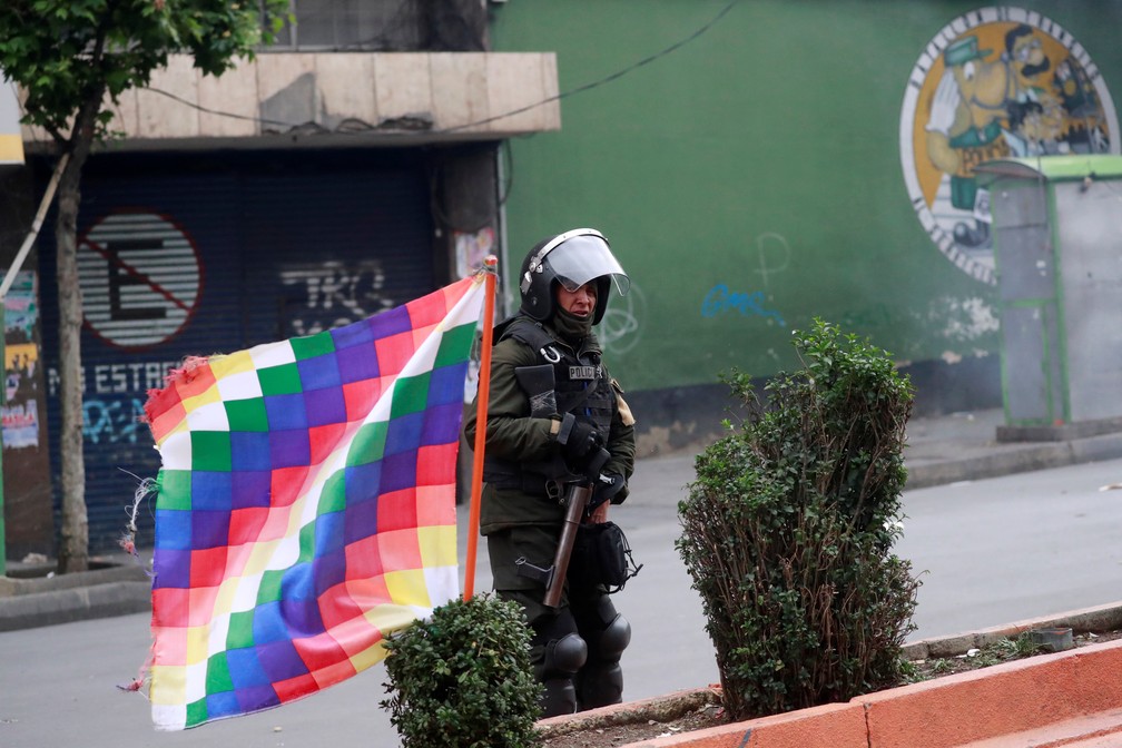 Atrás de uma bandeira wiphala, policial patrulha área de La Paz após confronto com manifestantes em mais um dia de protestos na Bolívia, na quarta-feira (13) — Foto: Henry Romero/Reuters