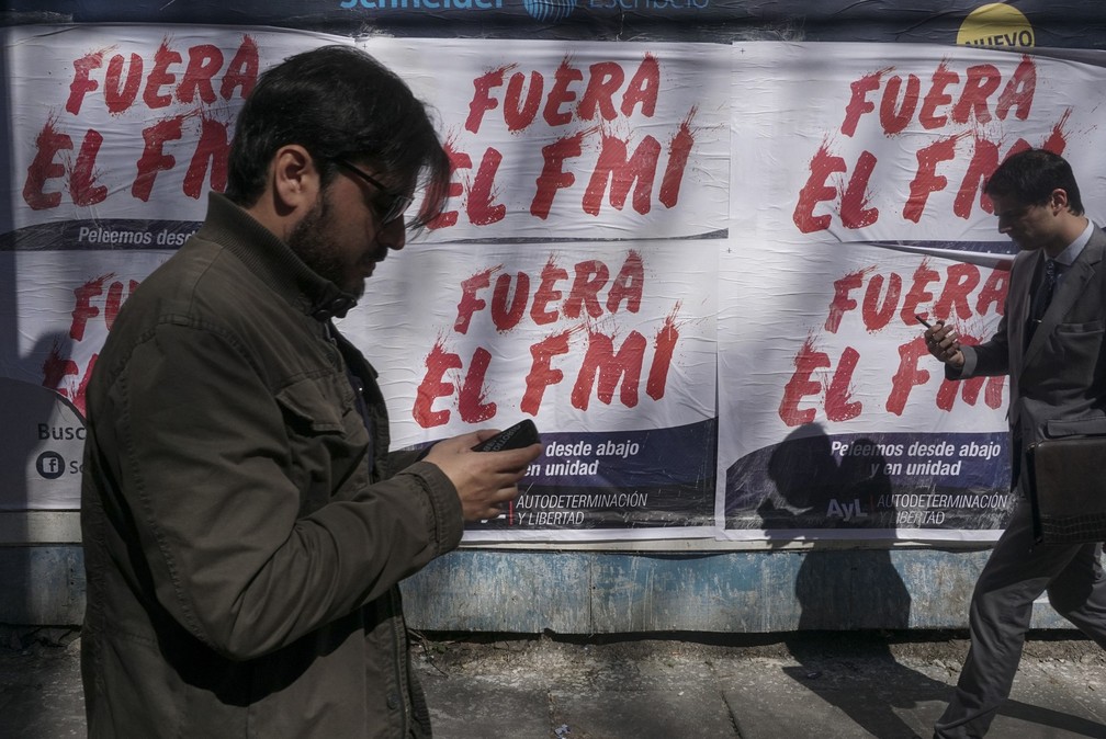 Homens caminham em frente a cartazes de protesto contra o FMI em Buenos Aires, na Argentina â€” Foto: Eitan Abramovich/AFP
