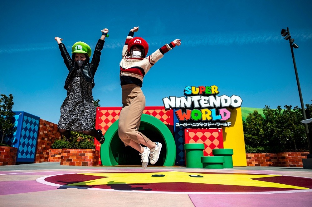 Duas visitantes com seus chapeus de Mario e Luigi saltam em frente ao túnel em forma de cano que dá acesso à área temática Super Nintendo World, do Universal Studio Japan AFP