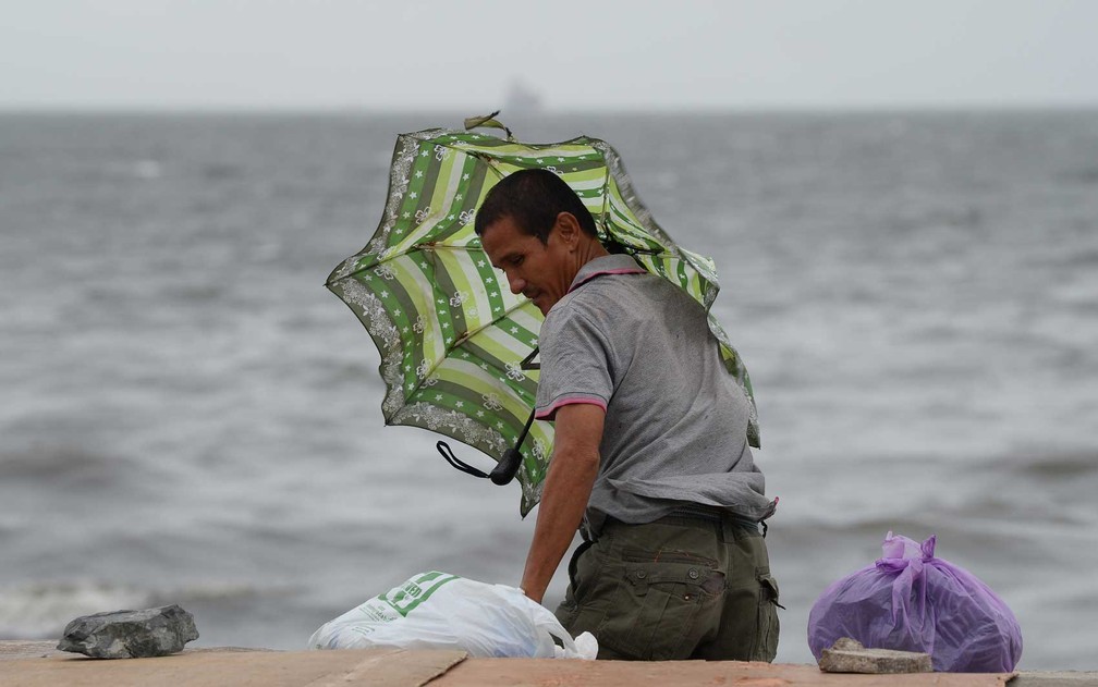 Um homem segura um guarda-chuva enquanto se refugia do vento e da chuva ao longo da baía em Manila, em 30 de outubro de 2018, quando o tufão Yutu atingiu o norte da capital. — Foto: Ted Aljibe / AFP