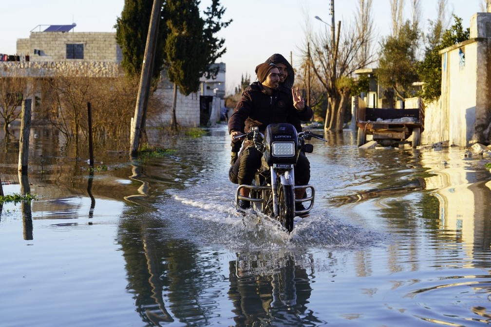 Uma motocicleta dirige por uma rua inundada na vila síria de Tloul, controlada pelos rebeldes, perto da fronteira com a Turquia, em 9 de fevereiro de 2023. — Foto: MUHAMMAD HAJ KADOUR / AFP
