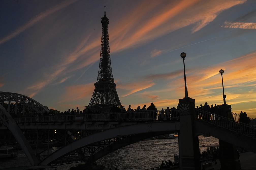 Grupo de pessoas se posicionam em ponte próxima à torre Eiffel, principal ponto turístico de Paris — Foto: Michel Euler/AP