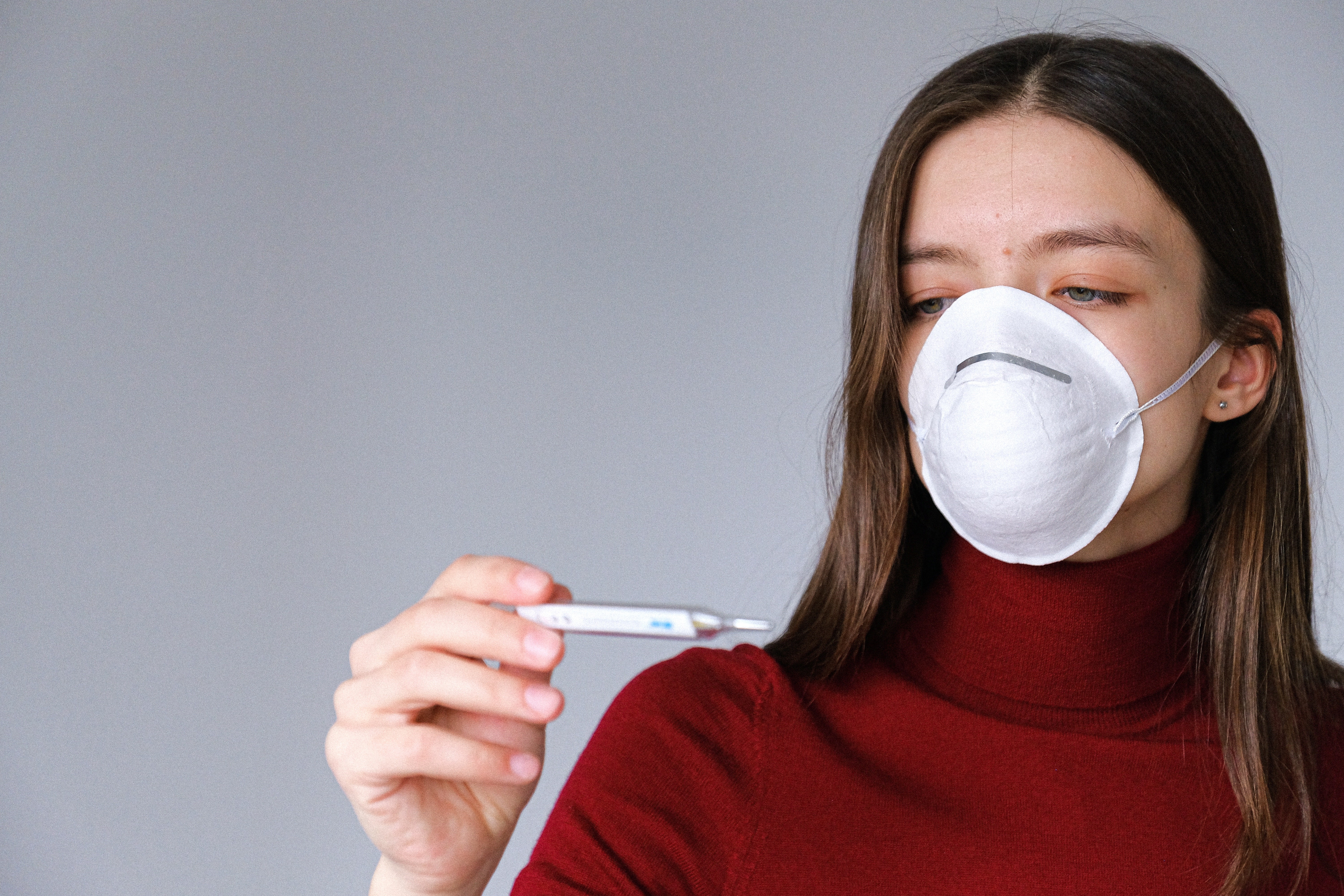 Febre e tosse são alguns dos principais sintomas da Covid-19. Acima: mulher usando máscara afere a temperatura (Foto: Anna Shvets/Pexels)