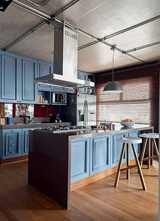 A cozinha deste triplex de 281 m² possui armário de madeira com inspiração londrina. No teto cinza, as instalações elétricas ficam aparentes.  Projeto do arquiteto Nelson Kabarite