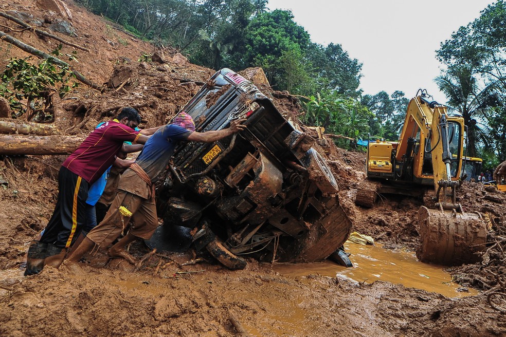 Equipes de resgate empurram veículo capotado  na lama e nos escombros em Kokkayar, no estado indiano de Kerala — Foto: AFP