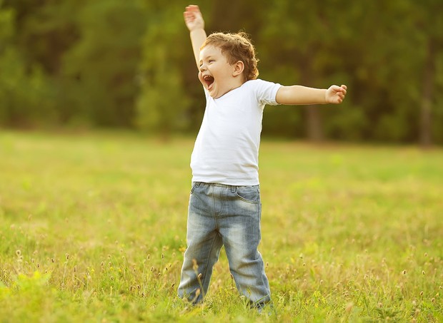 Criança feliz sorrindo e levantando os braços (Foto: Shutterstock)