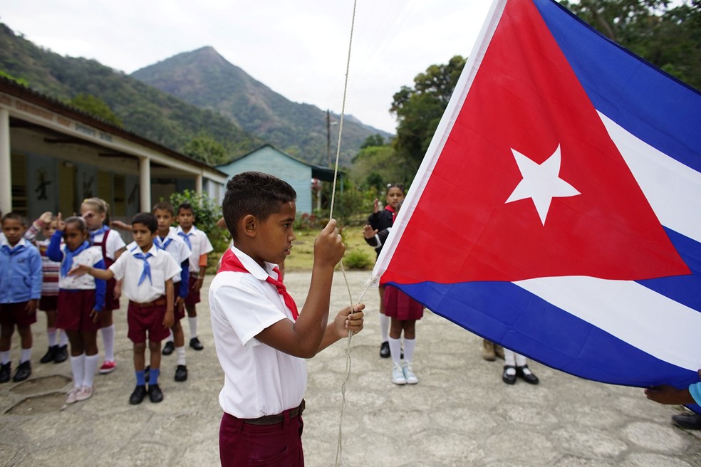 Menino hastea bandeira de Cuba durante cerimônia em escola de Santo Domingo, na Serra Maestra, em imagem de 2 de abril  (Foto: Alexandre Meneghini/ Reuters)