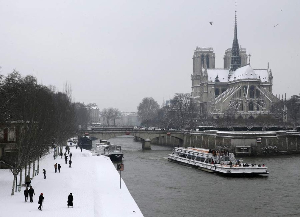 Barco turístico passa pelo rio Sena com a catedral de Notre Dame coberta de neve ao fundo — Foto: Christian Hartmann/Reuters