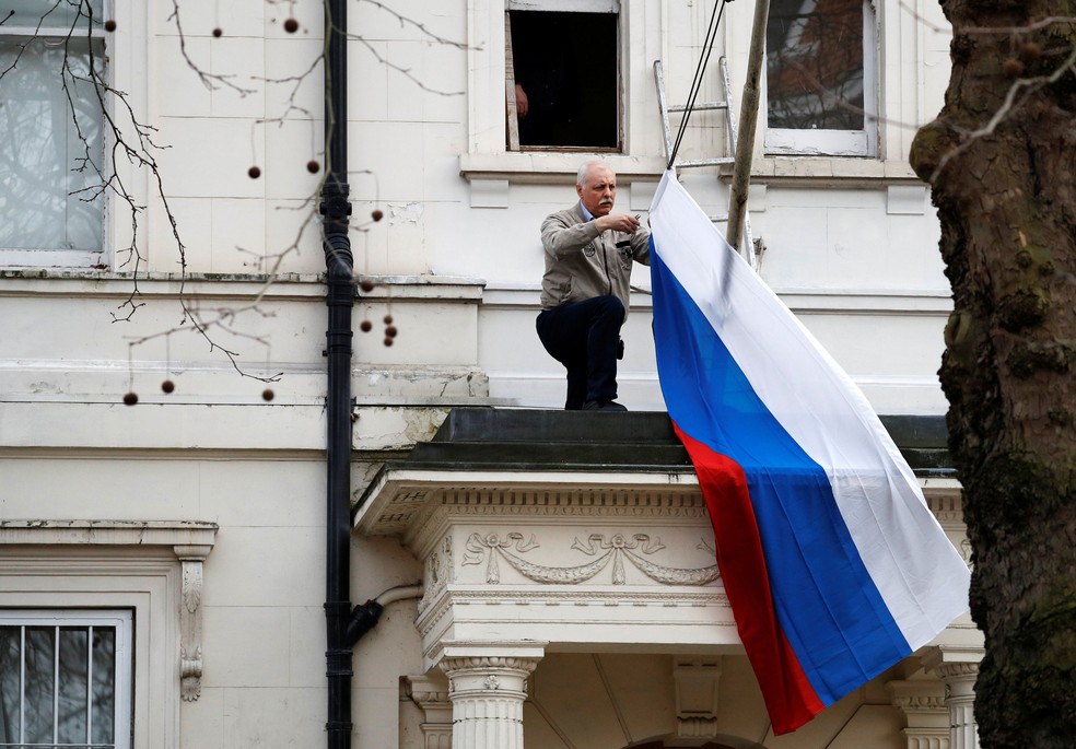 Homem retira bandeira russa da embaixada do país em Londres, nesta quarta-feira (14)  (Foto: Phil Noble/ Reuters)