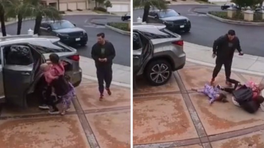 Mãe, que está cheia de mochilas, tenta retirar as filhas do carro e cai no chão, enquanto marido está no celular