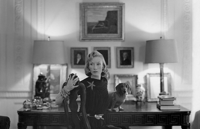Mrs. Huttleson (Millicent) Rogers seated at desk, wearing 1939 Alix jersey dress, with jewelry and a dachshund dog on the desk beside her. (Photo by John Rawlings/Condé Nast via Getty Images) (Foto: Conde Nast via Getty Images)