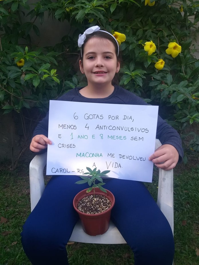 Caroline Pereira da Silva, de 10 anos, com uma muda de maconha e um cartaz onde explica como o uso diário do óleo artesanal mudou a sua vida. — Foto: Arquivo pessoal