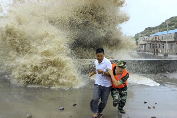 Guarda de fronteira ajuda homem a escapar de onda durante passagem do tufão Soulin em Wenzhou, na China (Foto: China Daily/Reuters)