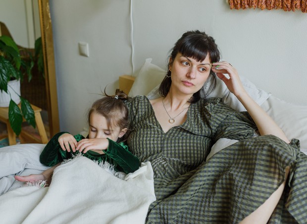Mãe cansada olhando para o lado com filha deitada (Foto: Ksenia Chernaya/ Pexels)