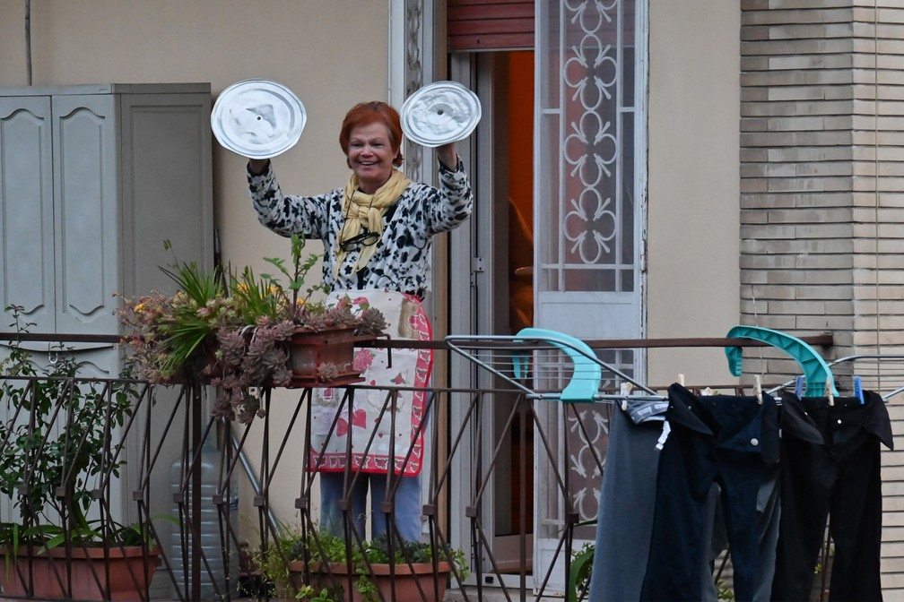 Uma moradora usa tampa de panelas durante um 'flashmob' chamado 'Olhe pela janela, minha Roma!' (Affacciati alla Finestra, Roma Mia!) durante isolamento para evitar a propagação do novo coronavírus em Roma, na Italia, em 13 de março  — Foto:  Andreas Solaro/AFP