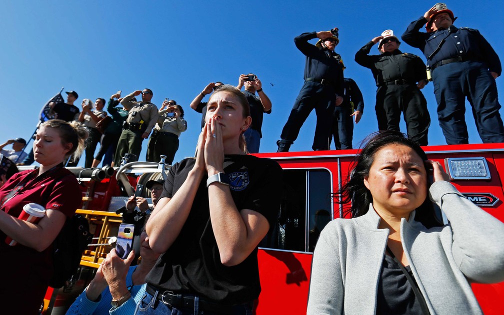 Mulheres à frente de um caminhão de bombeiros assistem ao cortejo do sargento Ron Helus, durante sua passagem pela Ventura Highway 101 em Thousand Oaks, na Califórnia, na quinta-feira (8) — Foto: Reuters/Mike Blake
