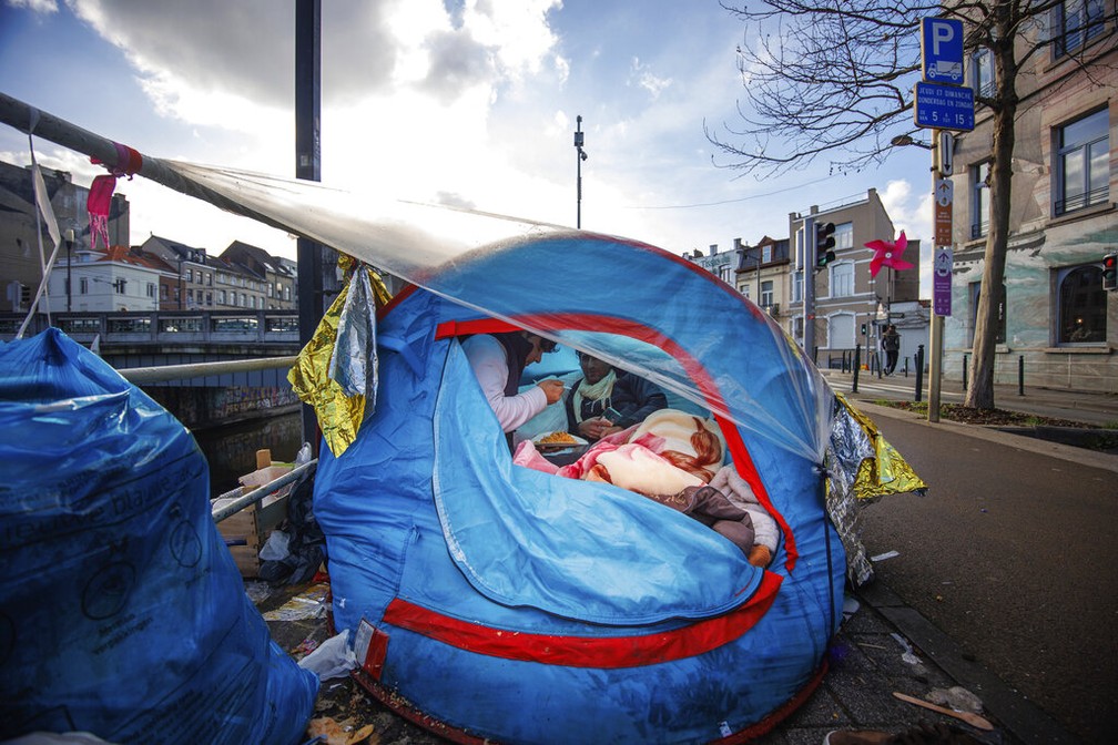 Dois homens compartilham uma refeição em um acampamento improvisado do lado de fora do centro de recepção Petit Chateau, em Bruxelas, Bélgica, terça-feira, 17 de janeiro de 2023. — Foto: Foto AP/Olivier Matthys