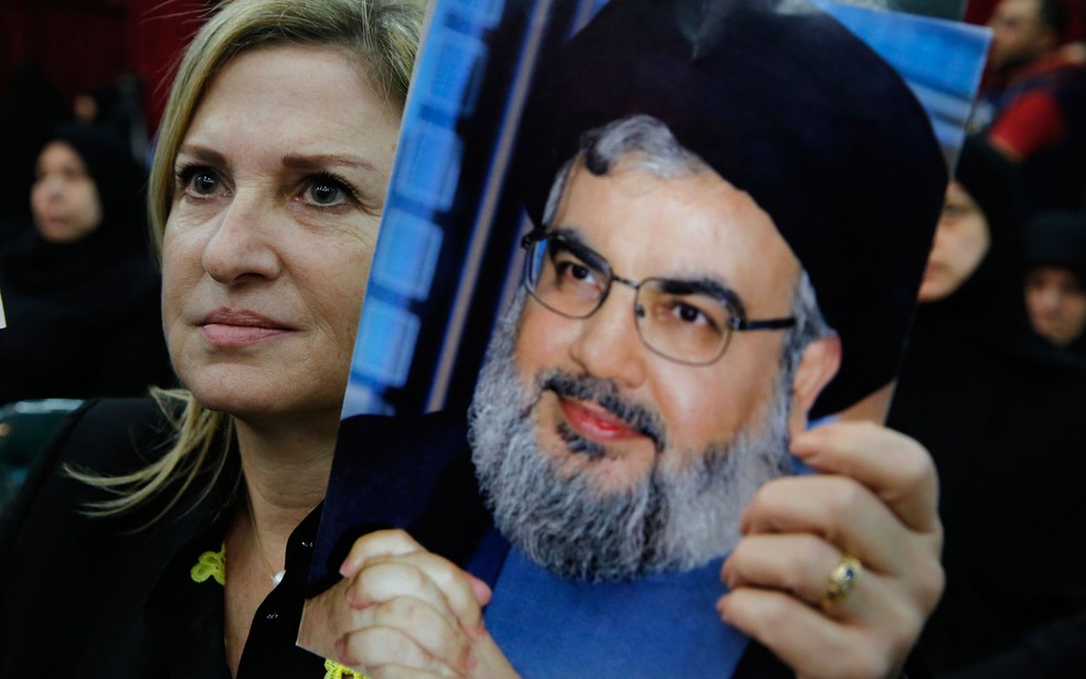 Mulher exibe foto do líder do Hezbolahh, Hassan Nasrallah, durante seu pronunciamento na TV libanesa, em Beirute, na sexta-feira (10) (Foto: AP Photo/Bilal Hussein)