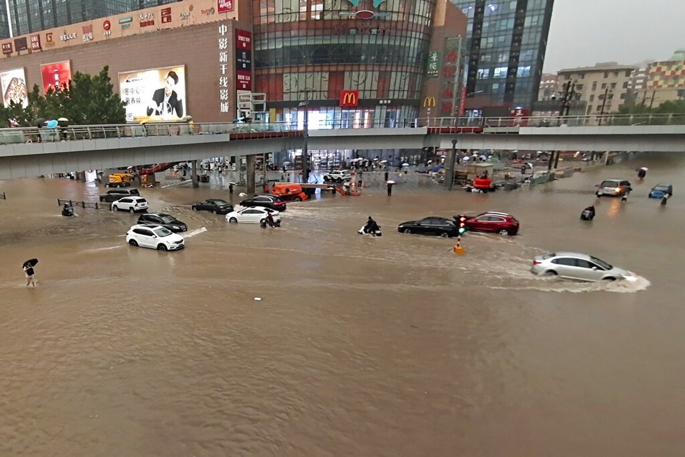 Carros tentam cruzar via inundada em frente a centro comercial de Zhengzhou, na China, em 20 de julho de 2021 — Foto: Chinatopix/AP