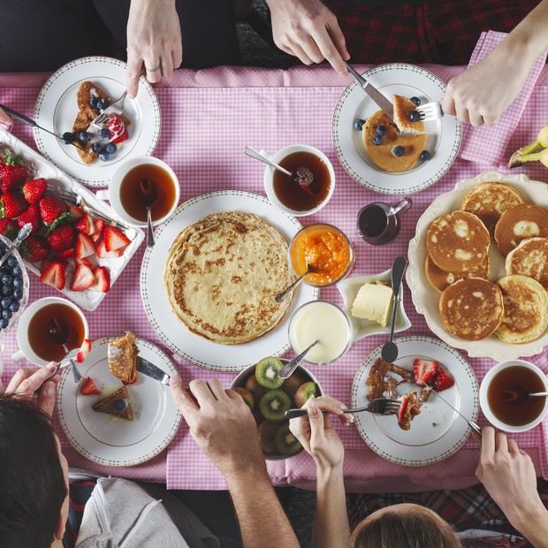 Breakfast table. Flat lay of eating peoples hands over breakfast table with crepes, pancakes, tea and berries. Top view (Foto: Getty Images)