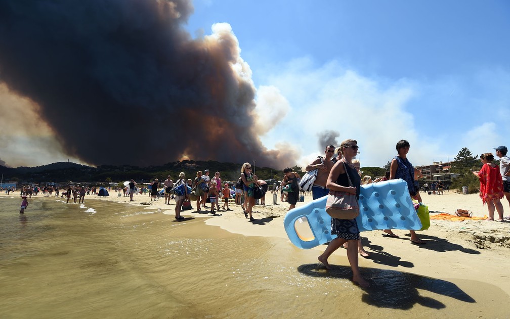 Banhistas deixam praia enquanto observam incêndio florestal em Bormes-les-Mimosas, na França, na quarta-feira (26) (Foto: Anne-Christine Poujoulat/AFP)