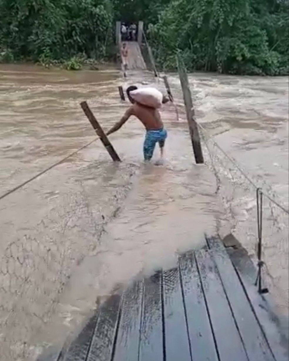 Moradores se arriscam em ponte quebrada para conseguir utensílios para a comunidade — Foto: Reprodução