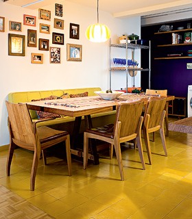 Os ladrilhos estampados da cozinha invadem a sala de jantar. No entanto, neste ambiente, eles perdem as estampas e ficam apenas com o fundo amarelo, mesma cor do sofá que substitui as cadeiras da mesa. Projeto do estúdio SuperLimão
