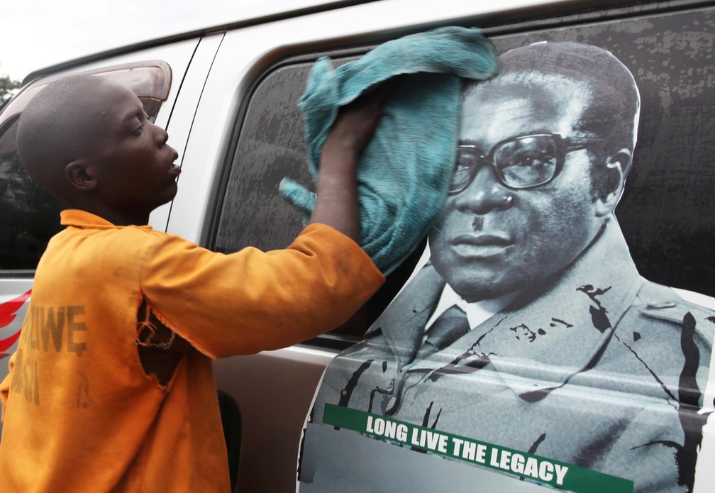 Jovem lava um ônibus com foto do presidente Robert Mugabe em um terminal em Harare — Foto: Philimon Bulaway / Reuters
