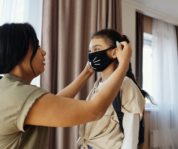 Mãe colocando máscara estampada na filha (Foto: Pexels)