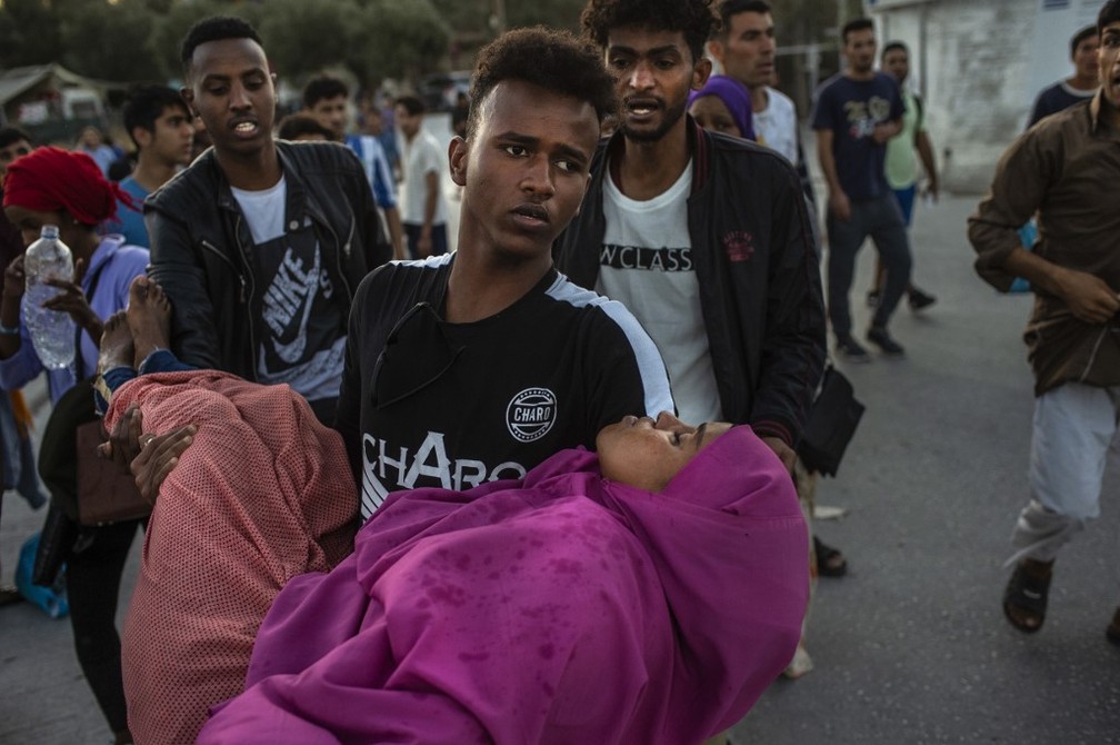 Migrante carrega mulher ferida em confronto com a polícia em acampamento na ilha de Lesbos, na Grécia, neste domingo (29) — Foto: Angelos Tzortzinis/AFP