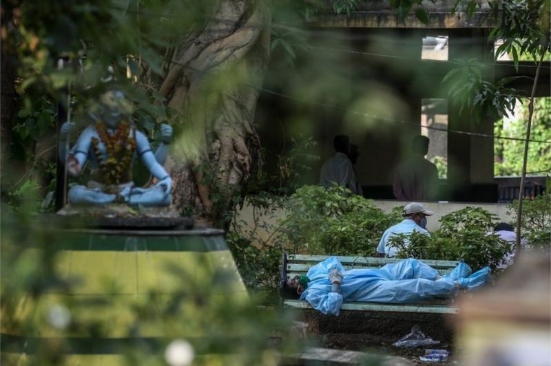 Um familiar exausto antes de realizar os últimos ritos para vítimas da covid em um campo de cremação em Vasai, nos arredores de Mumbai, Índia (Foto: EPA via BBC)