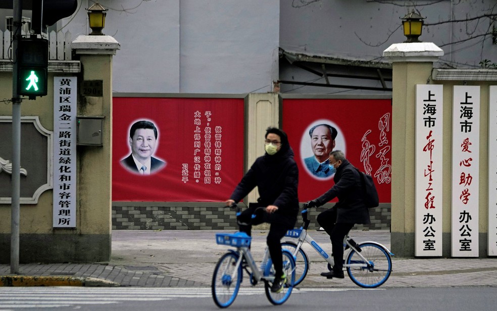 10 de fevereiro: Ciclistas com máscaras para proteger contra o coronavírus passam em frente a retratos de Xi Jinping e Mao Zedung em Xangai, na China.  — Foto: Aly Song/Reuters