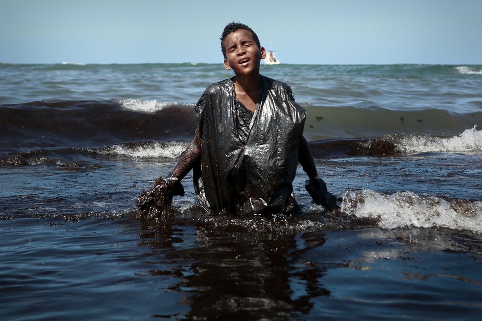 Menino protege o corpo com sacos de lixo ao retirar petróleo na praia de Itapuama, em Cabo de Santo Agostinho, Pernambuco — Foto: Leo Malafaia/AFP