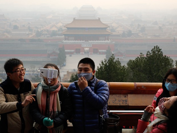 Turistas, alguns usando máscaras para se proteger da poluição, tiram uma selfie no Parque Jingshan em um dia poluído em Pequim, na China (Foto: Andy Wong/AP)