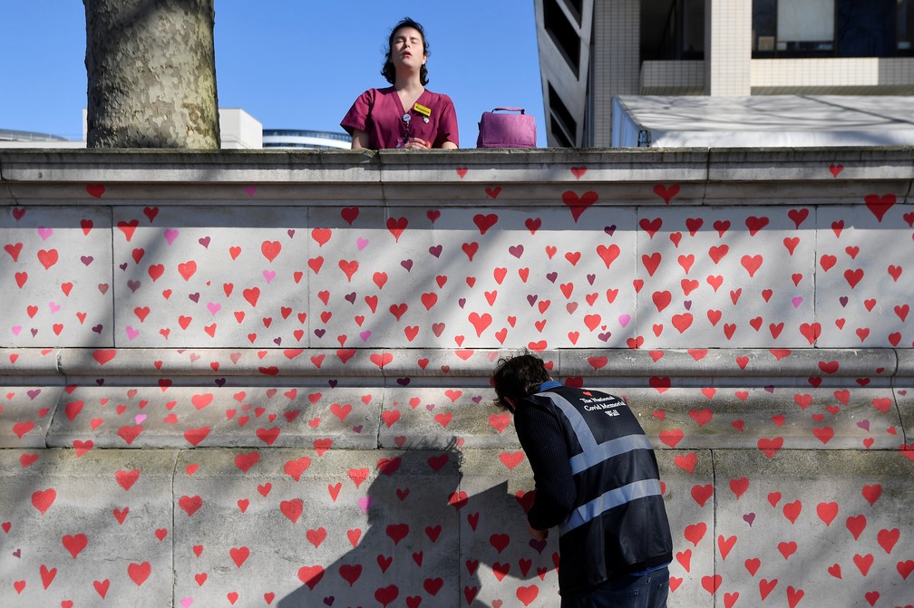 Trabalhadora de saúde do hospital St Thomas atrás da parede pintada em corações — Foto: Toby Melville/Reuters