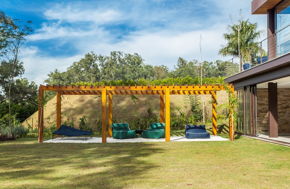 Uma extensão da área de lazer da casa em Itu, SP, o pergolado é um ambiente descontraído para relaxar. Para criar essa atmosfera, o escritório Korman Arquitetos escolheu pufes em diferentes formatos e cores — Foto: Eduardo Pozella