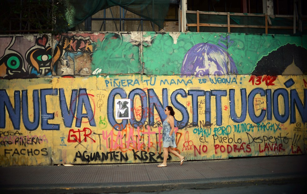 Mulher passa por um grafite que pede uma nova Constituição em Santiago, no Chile  — Foto: Rodrigo Arangua / AFP