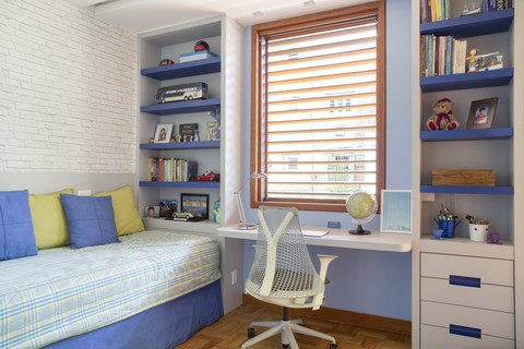 ​Neste quarto, a arquiteta Patricia Netto desenhou a marcenaria branca, com detalhes em azul. A escrivaninha foi posicionada, estratégicamente, embaixo da janela, onde entra bastante iluminação natural. O papel de parede, ao lado da cama, simula tijolinhos, o que leva charme ao ambiente