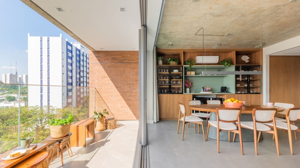 DÚPLEX DE RENATA: A vista da varanda revela parte da área de jantar, com cadeiras de madeira clara e a estante projetada pelo arquiteto e executada sob medida — Foto: Guilherme Pucci
