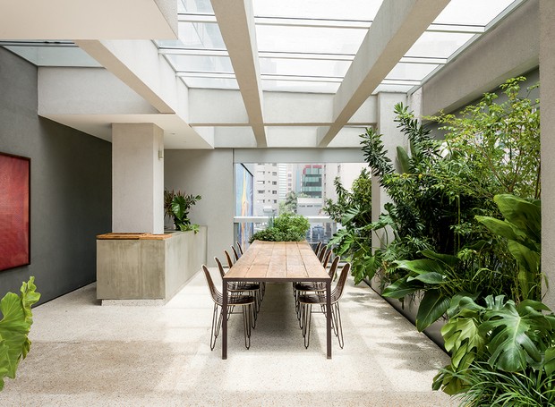 A pérgola de concreto é coberta por vidro em apenas 43 m² do terraço onde fica o espaço gourmet. A cozinha aberta tem bancada com placas de concreto em cima e nas laterais (Foto: Ricardo Bassetti / Divulgação)