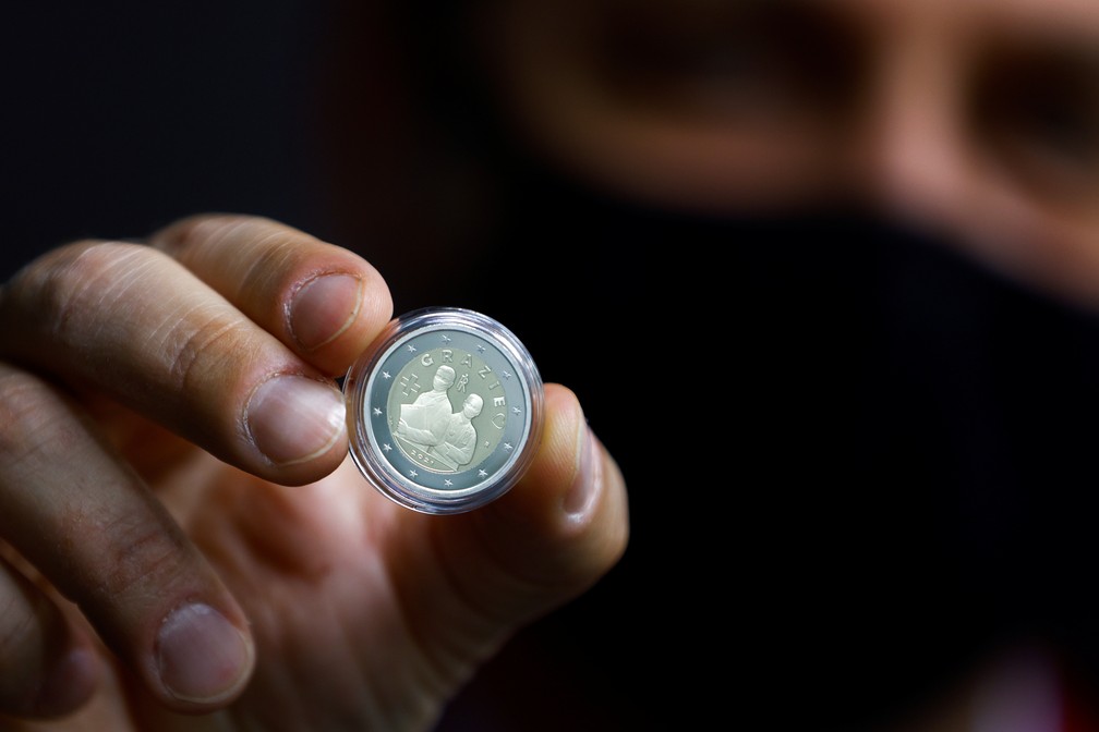 Homem mostra a moeda comemorativa de 2 euros, em homenagem aos profissionais de saúde durante a pandemia da doença do coronavírus. — Foto: REUTERS/Guglielmo Mangiapane