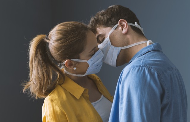 Young millennials couple wearing protective face masks and kissing each other, virus spread prevention and people concept (Foto: Getty Images/iStockphoto)