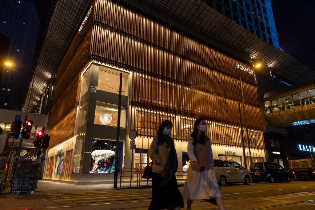 Pedestres de máscara caminham em frente a uma loja da Hermès em Hong Kong (Foto: Getty)