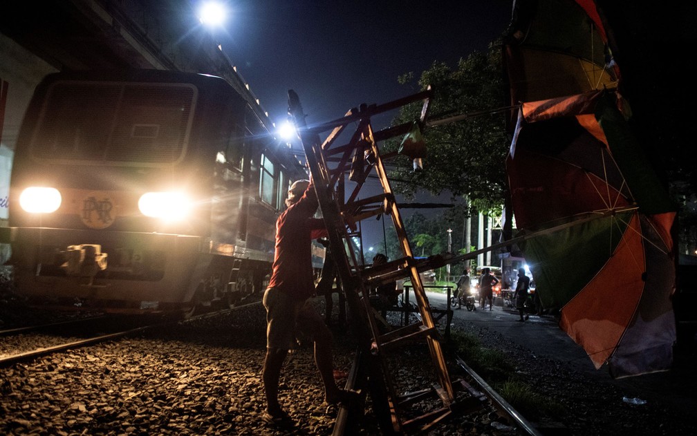 Um empurrador levanta seu carrinho enquanto um trem passa pela linha em Manila, em foto de 19 de outubro — Foto: Noel Celis/AFP