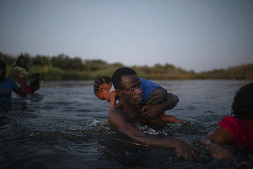 Imigrante atravessa o Rio Grande para chegar aos EUA com uma criança no ombro, em 20 de setembro de 2021 — Foto: Felix Marquez/AP