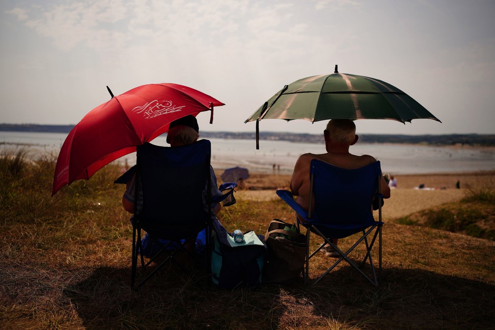 Dois idosos se abrigam debaixo de guarda-chuvas em uma praia na Cornualha, no extremo sudoeste da Inglaterra. — Foto: Ben Birchall/PA via AP