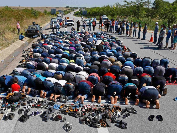Refugiados fazem oração em rodovia perto da cidade de Edirne, na Turquia, nesta sexta (18) (Foto: Osman Orsal/Reuters)