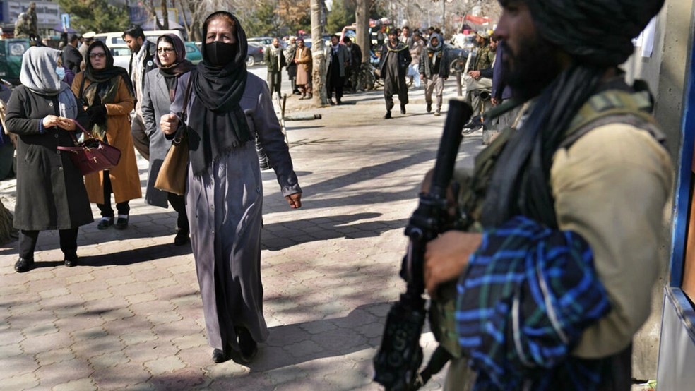 Mulheres afegãs passam por um combatente do Talibã em Cabul, Afeganistão. As vidas de afegãs estão sendo destruídas pela repressão do Talibã a seus direitos básicos, informou a Anistia Internacional em um novo relatório publicado nesta quarta-feira, 27 de julho de 2022. — Foto: AP - Hussein Malla