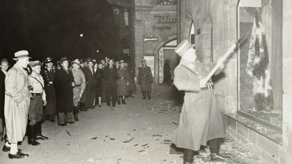 Pessoas observam oficial nazista atacar loja de um judeu — Foto: YAD VASHEM PHOTO ARCHIVE/via BBC