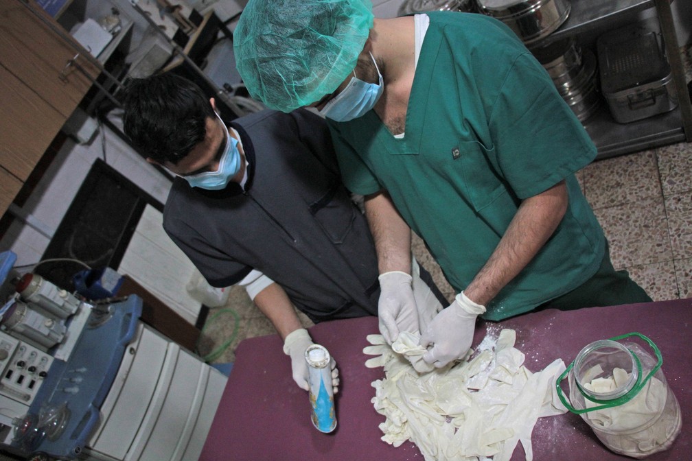 Equipe médica esteriliza luvas usadas em cirurgia para serem reutilizadas em hospital em Duma, na Síria  (Foto: Hamza Al-Ajweh/AFP)